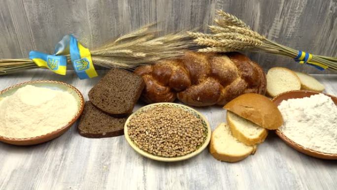 桌子上摆放着面包制品和盛有面粉和小麦的盘子，背景是装饰着乌克兰国家象征的小麦和黑麦穗