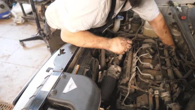 修理工的脏手在车间或维修厂修理汽车的发动机。汽车修理工在车库检查电机的引擎盖下工作。维护和汽车诊断的