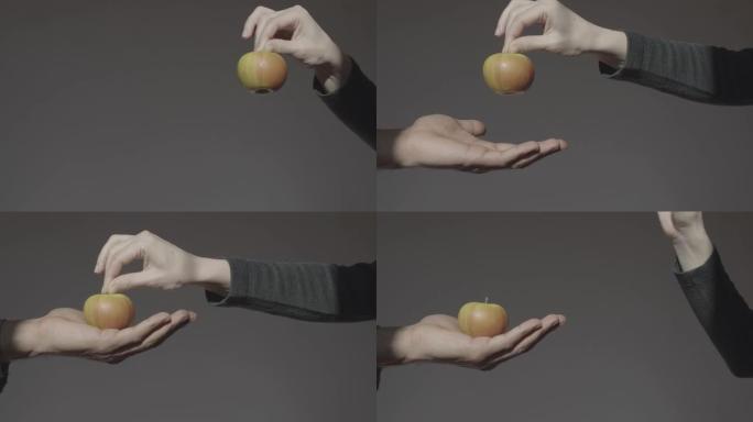 黑暗背景上的一只手伸出一个绿色的苹果，抓住它的茎。另一只手拿着它，握在你的手掌里。不和谐的苹果。