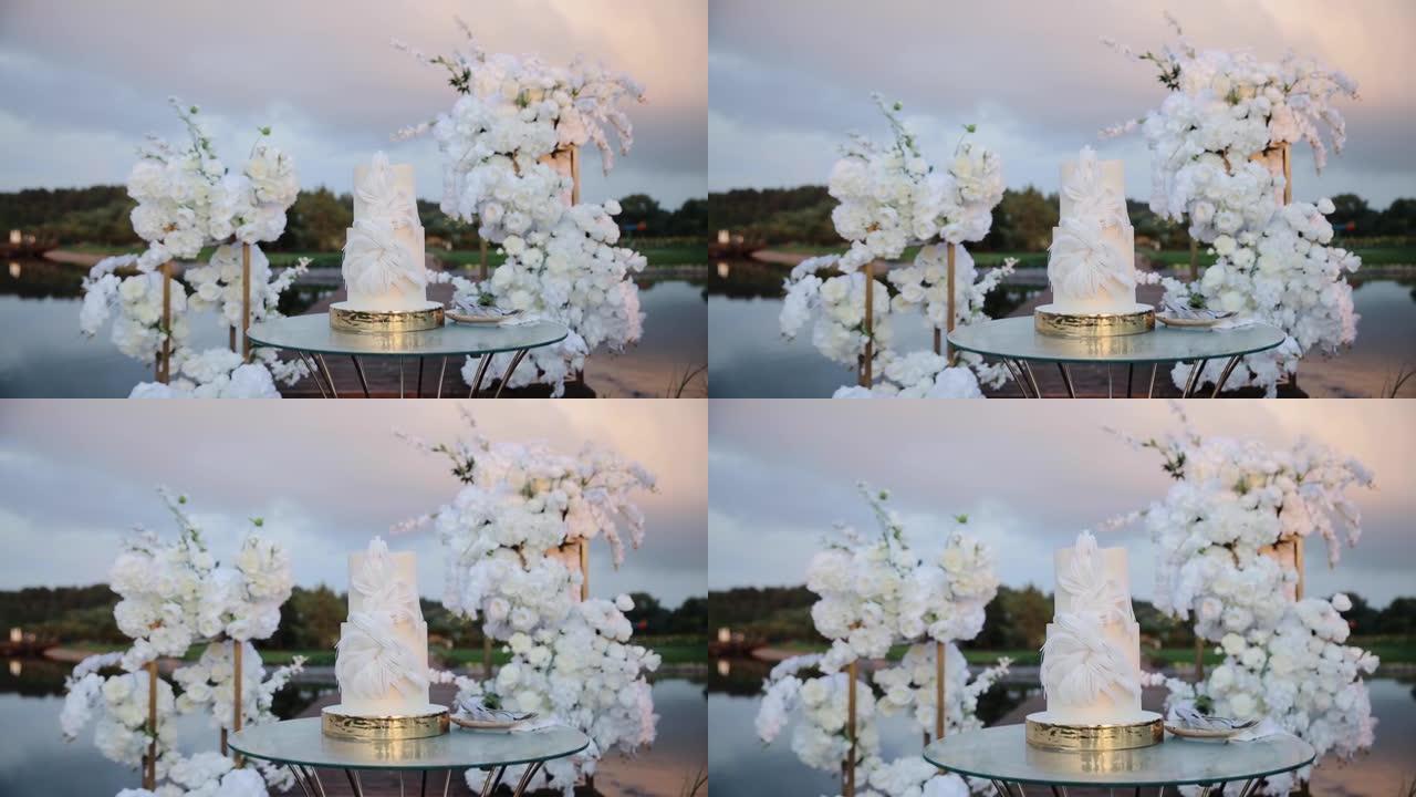 婚礼蛋糕在礼仪区特写。带有创意装饰的白色结婚蛋糕。该地点为湖附近的婚礼派对装饰。慢动作