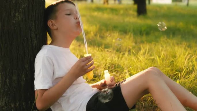 儿童男孩吹肥皂泡，在夕阳下在公园玩耍。孩子在夏天的花园里玩肥皂泡。快乐童年理念