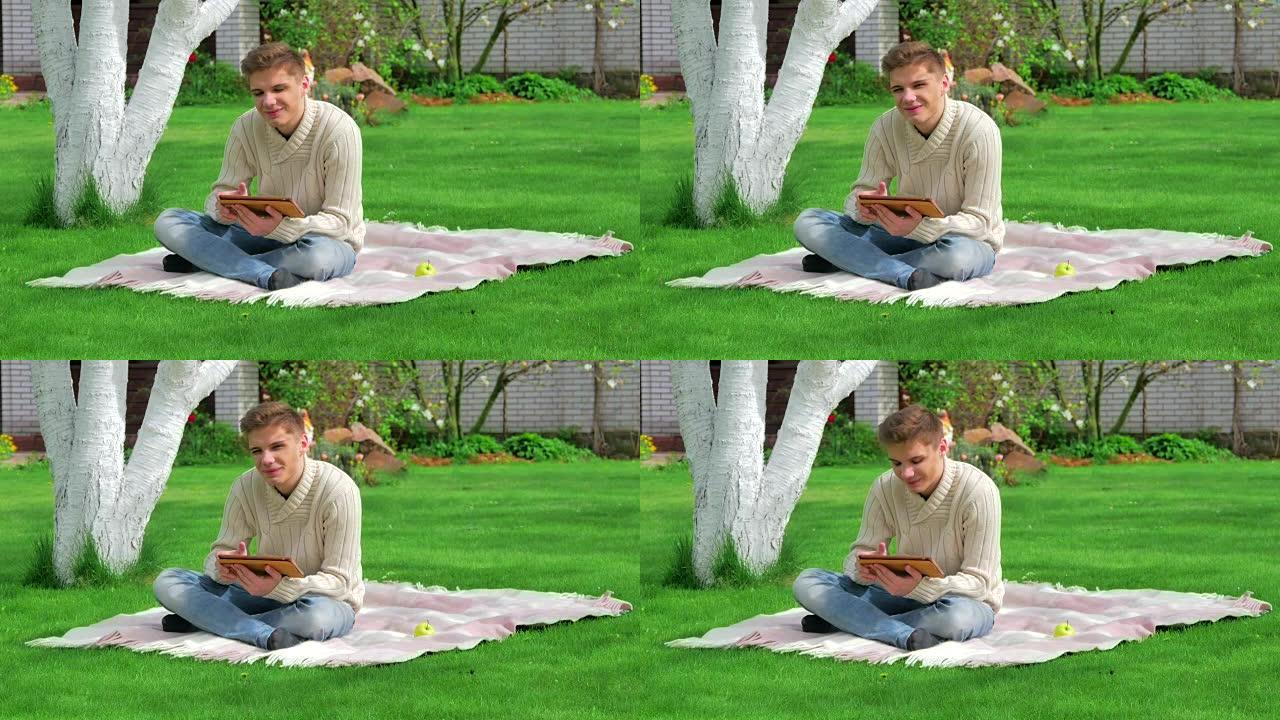 拿着数字平板电脑坐在草坪上的家伙