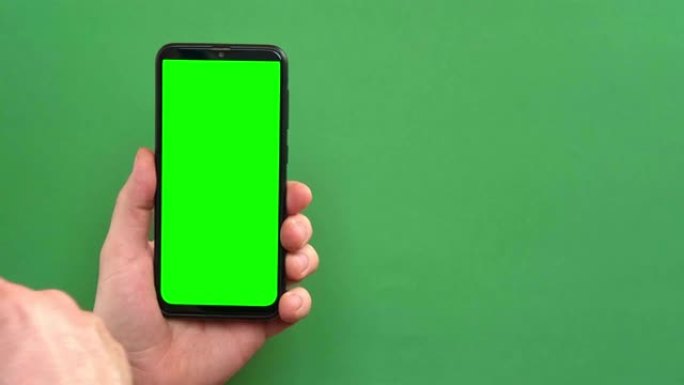 年轻人的手在绿色背景上使用带有绿色屏幕的智能手机。手势包。男性手触摸，点击，点击在黑色手机chrom