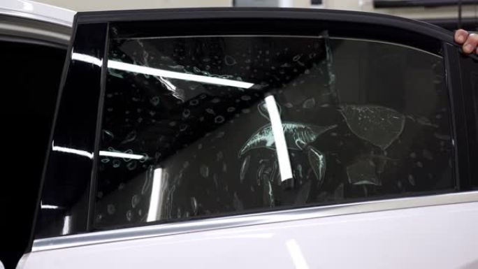 一位特写机械师在汽车玻璃上安装了一层着色膜，他用刮刀。