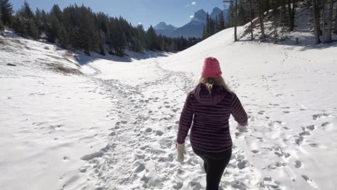 成熟的女人在高山环境中沿着雪道行走