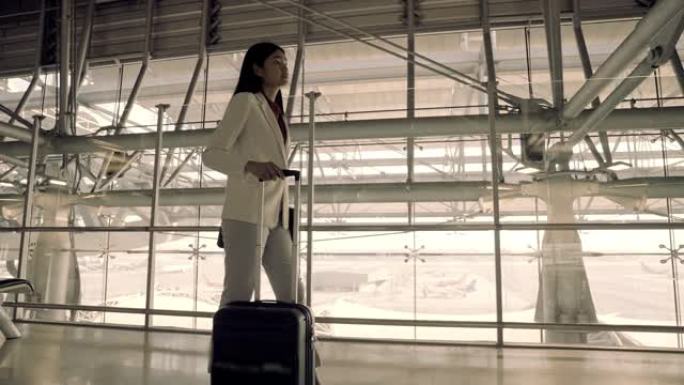 旅行保险带旅行，商务妇女在机场带着手提箱散步，商务旅行。背光色调。