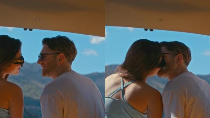 亲爱的夫妇在湖边的一个大汽车后备箱里休息和露营。欣赏绿松石湖景和亲吻垂直视频