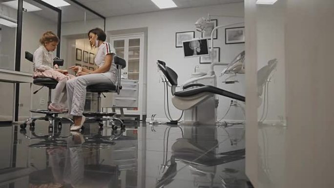 在牙医办公室正畸医生的背景下，一个小女孩的x射线头在安装牙套后学习刷牙。牙医为牙齿清洁进行咨询