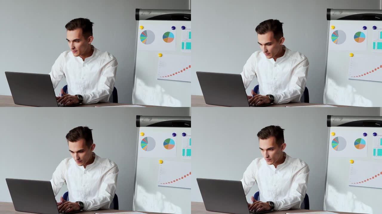 一位欧洲男性的肖像坐在办公室的笔记本电脑上，白色衬衫在图表和桌子的背景上
