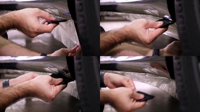 汽车修理工的特写镜头将保护膜涂在车身上。