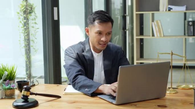 亚裔男子律师肖像在使用计算机和笔记本上班前为客户研究案件