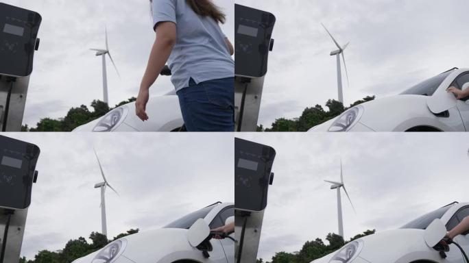 进步女性从风力涡轮机产生的充电站为电动汽车充电。