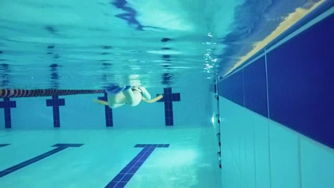 高级女子在游泳池用特殊设备游泳-水下
