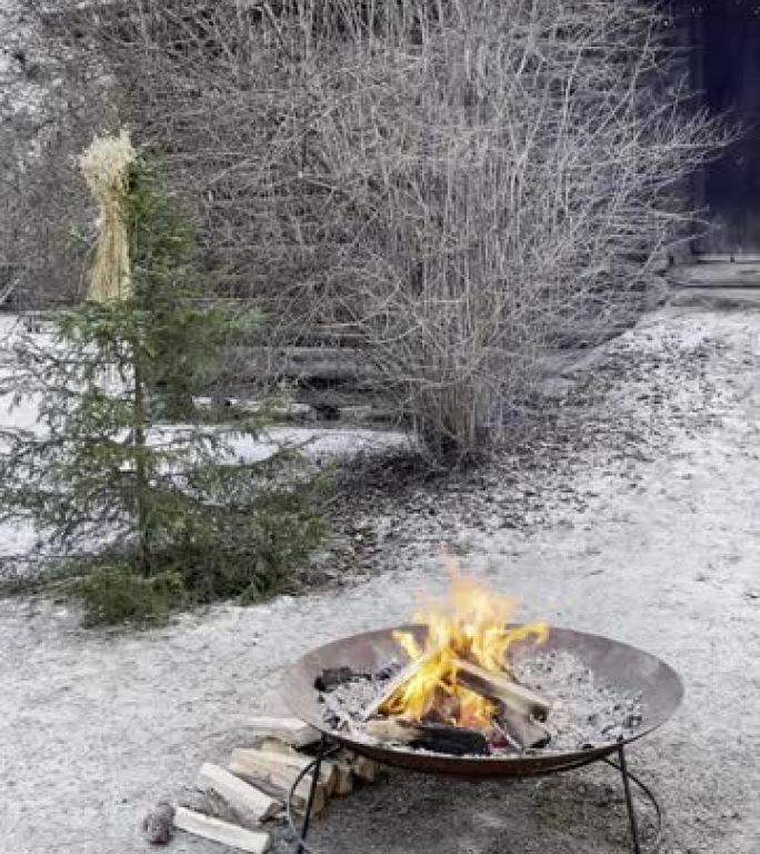 冬天下雪时，火盆或碗里的火在一年中最寒冷的月份传递着温暖和舒适。背景中的木屋让人想起了古老的维京人住
