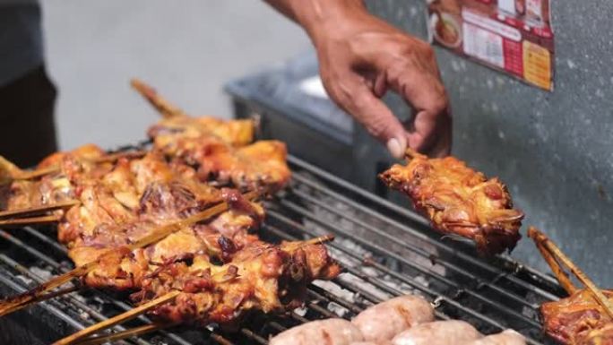 雄性手在明火或烤架上用短的细竹串烧烤各种肉。亚洲食品市场。