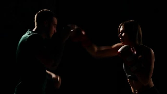 肌肉健身的女孩与他的教练一起训练，用拳击手套对脚进行打击。自卫的教训。拳击锻炼