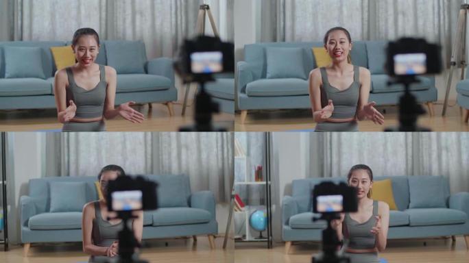 年轻的亚洲教练女性穿着运动服挥舞着手，对着镜头说话，一边在家录制教学练习