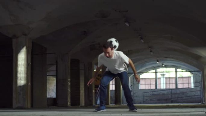 职业足球运动员用球表演自由式技巧的动作镜头。自信的年轻足球运动员在夏日的地下停车场炫耀杂耍技巧