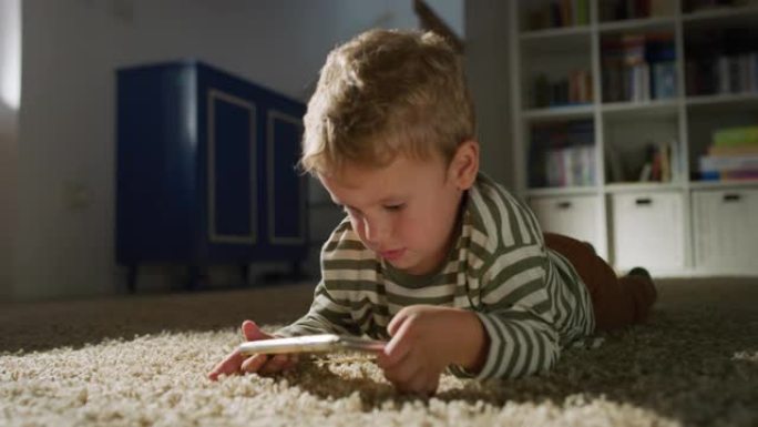 一个小男孩在客厅的智能手机上观看视频的肖像。好奇的男孩使用电话，玩手机教育游戏。纯真与童年的概念