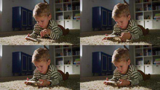 一个小男孩在客厅的智能手机上观看视频的肖像。好奇的男孩使用电话，玩手机教育游戏。纯真与童年的概念