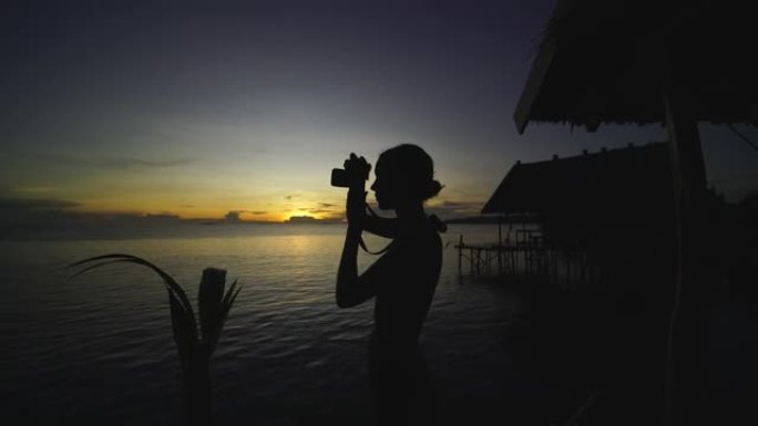 一名妇女在日落时在海滩上拍照的剪影