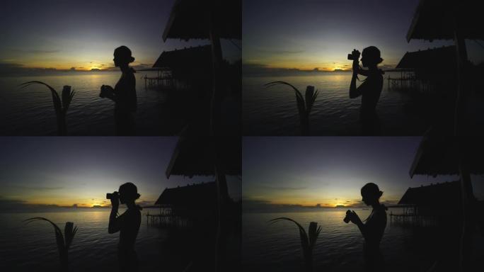 一名妇女在日落时在海滩上拍照的剪影