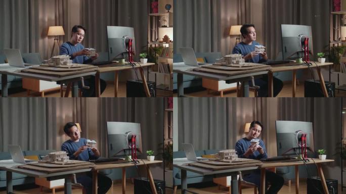 亚洲男工程师拿着并看着带有太阳能电池板的小房子模型，然后将其与家里桌面上的图片进行比较