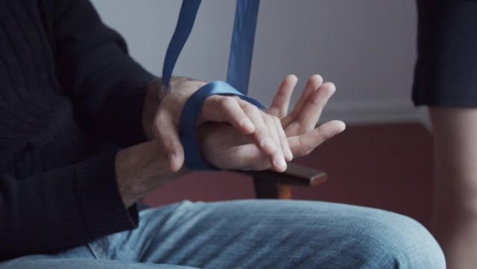 男性手被蓝色丝带包裹的特写。女人的手解开镣铐，男人张开手掌。心理上的类比。