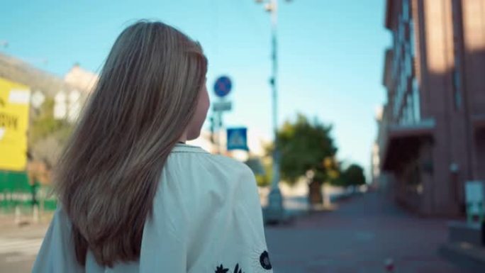 背面侧视穿着刺绣乌克兰衣服的少女在城市街道上慢动作环顾四周。自信的黑发少年在城市的户外漫步。