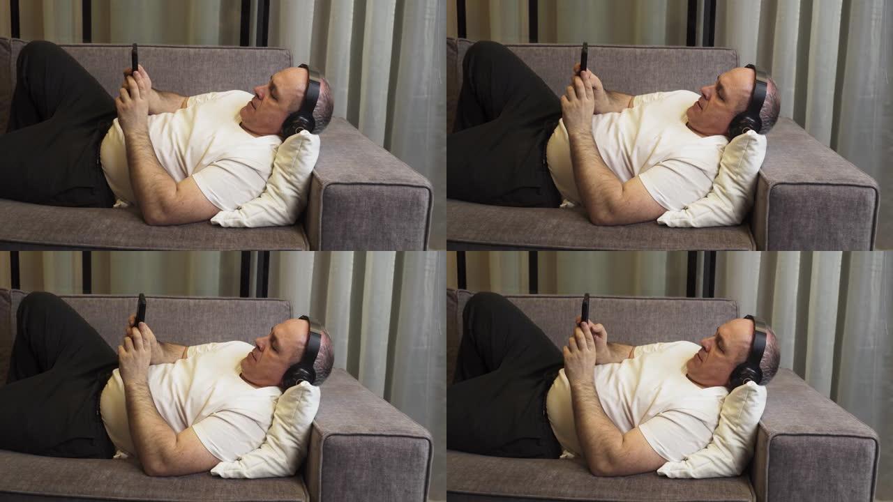 一个男人躺在沙发上，戴着耳机听音乐，看着电话