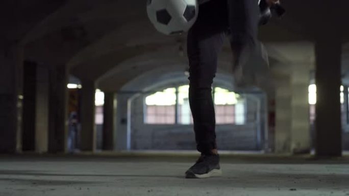 低角度，地面水平射击: 专注于有才华的年轻足球运动员的腿，熟练地玩弄球。男子在地下停车场展示他的自由