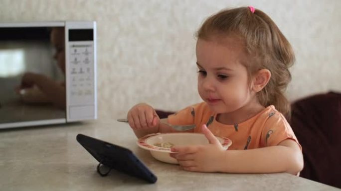 一个3岁的孩子用智能手机吃饭和看动画片。坏习惯。真实的场景。