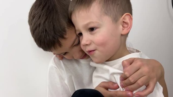 两个兄弟微笑并拥抱一个男孩4-5岁第二个8-9他们在白色背景上穿着白色t恤感到幸福和快乐家庭友谊兄弟