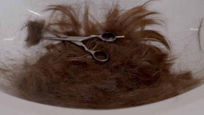 长发一束剪发的卷发躺在水槽里。手把剪刀