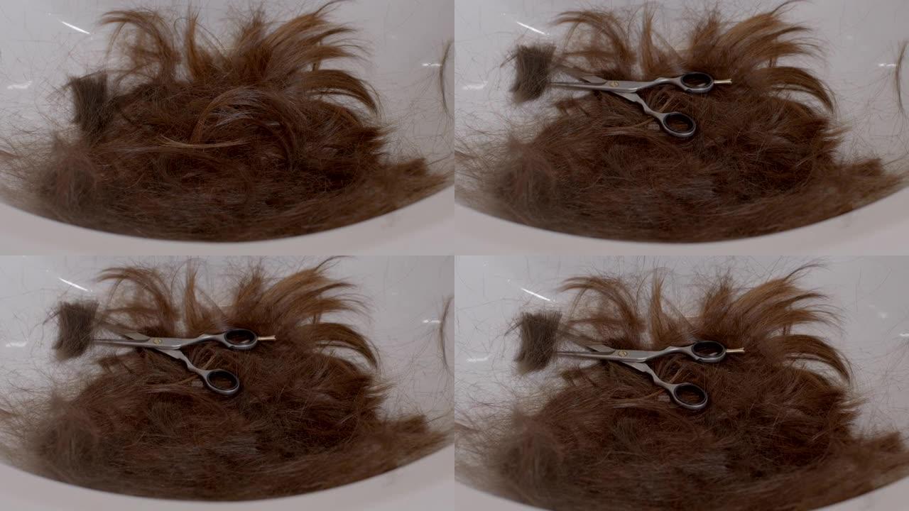 长发一束剪发的卷发躺在水槽里。手把剪刀