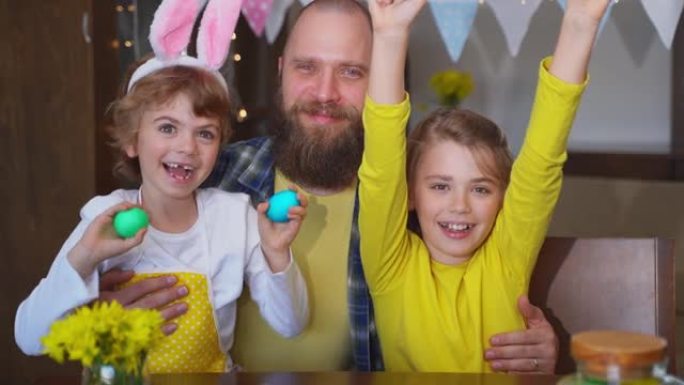 复活节家庭传统。父亲和两个白种人快乐的孩子，他们的兔子耳朵在家里坐在一起，玩复活节装饰的鸡蛋。