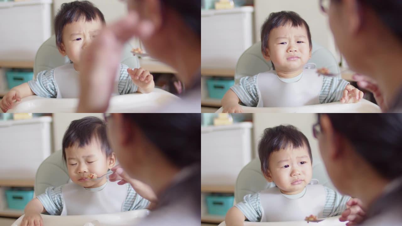 年轻的亚洲男婴在家里的午餐时间坐在椅子上时，母亲哭着拒绝吃饭或食物。儿童日常生活方式照顾或幼儿营养食
