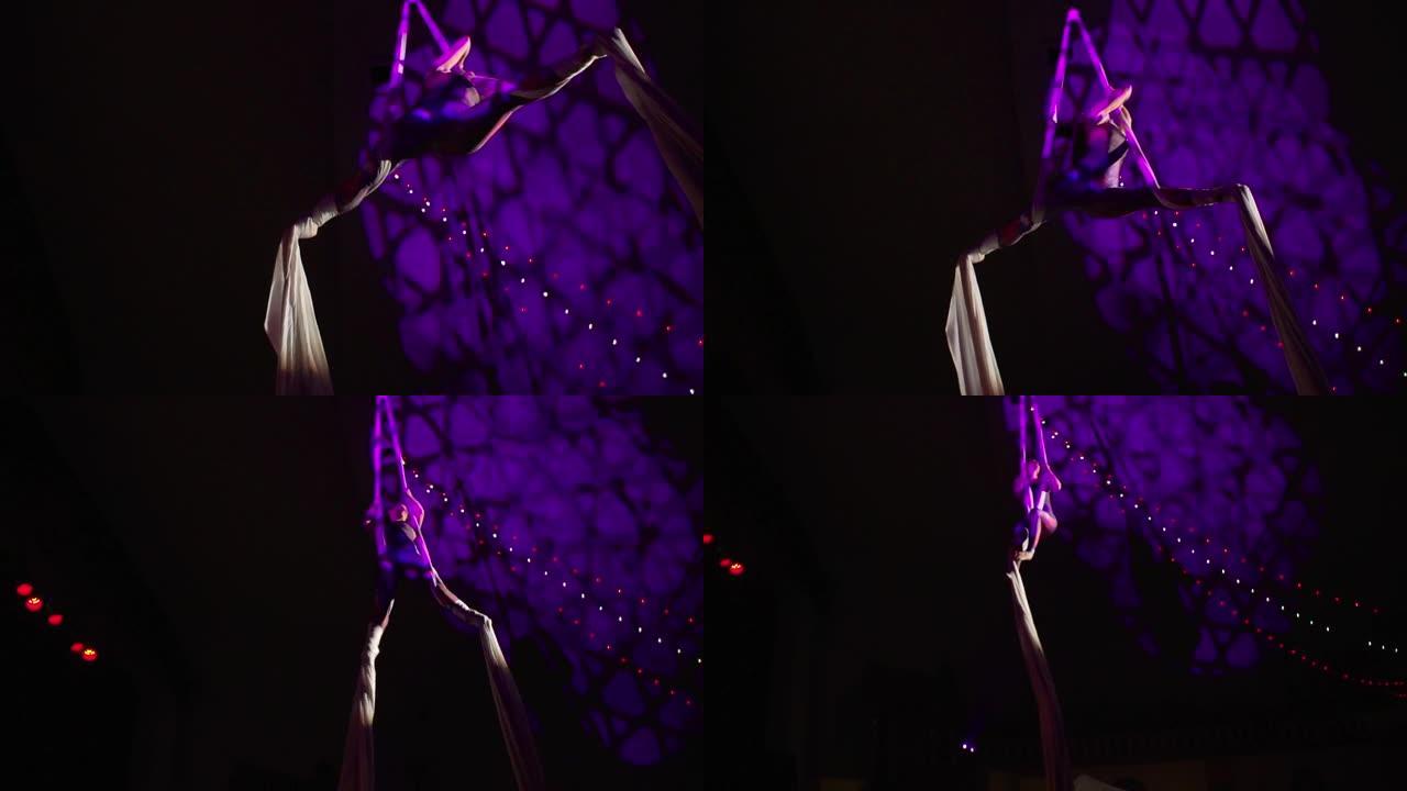 紫色灯光下敏捷的空中丝绸表演者的美丽表演
