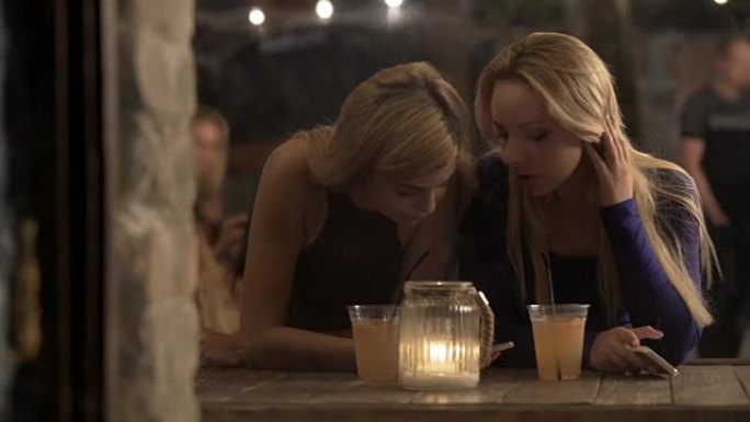 年轻女性在酒吧闲逛和喝酒，在智能手机上在线聊天