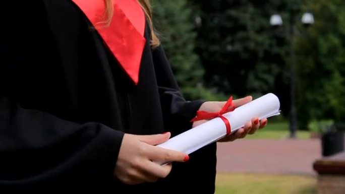 穿着学术服装的年轻女子拿着文凭，享受毕业典礼