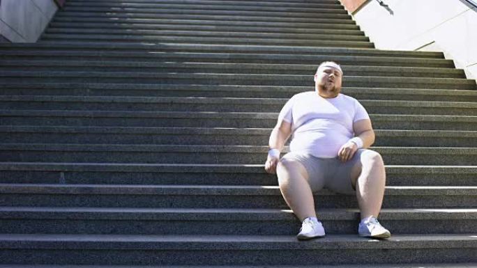 肥胖男子坐在楼梯上休息一分钟，锻炼后筋疲力尽