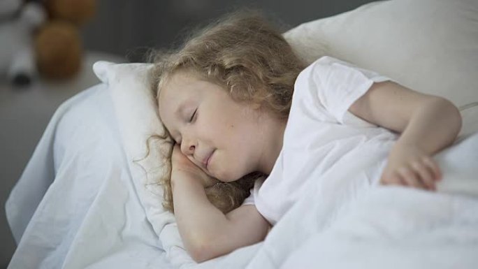 快乐的年轻女孩在温暖的床上享受好梦，孩子在睡觉时微笑