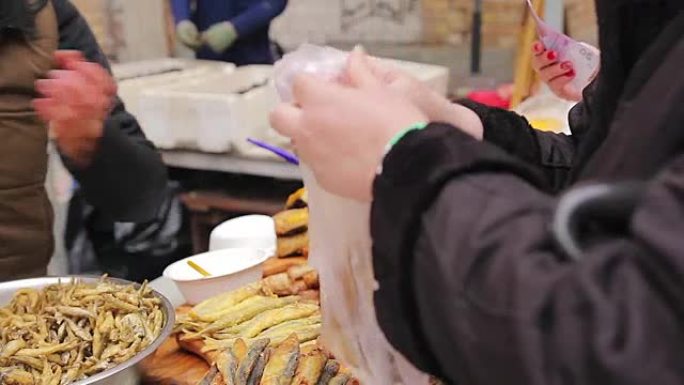 女人在街头食品店买脆皮零食。烤海鲜，