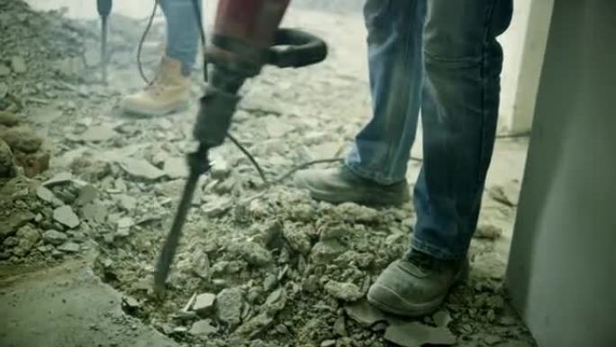 两名工人用手提凿岩机将混凝土地板打碎。