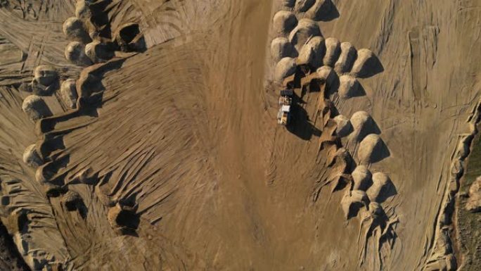 露天砂矿的Arial视图。前装载机从桩上装载沙子。在采石场工作的重型采矿机械。许多车轮轨道和成堆的沙