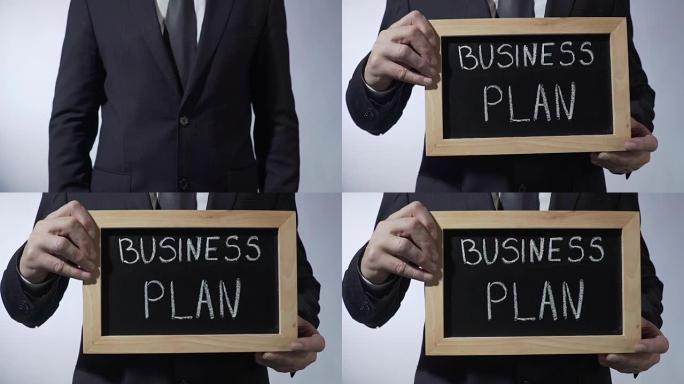 黑板上写的商业计划书，男性手举标志，策略，目标