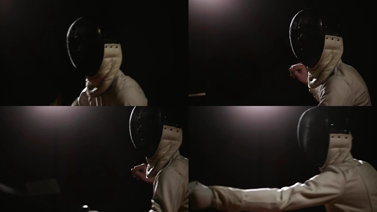 一个男人的特写镜头戴着头盔，用剑杆在黑暗的背景上与对手击剑。摄像机从上到下移动