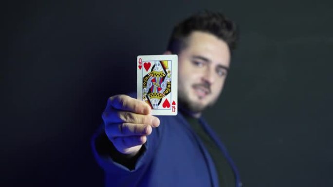 一位年轻魔术师在黑暗中模糊的视频肖像，在他的手掌中显示了一张隐藏的卡片，同时看着相机并露出它。显示的