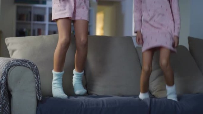 晚上，两个穿着相配的睡衣的小女孩在沙发上跳来跳去。女生一起玩。活跃的孩子玩得开心。纯真与童年的概念
