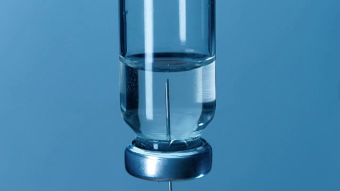 注射器的针头从蓝色背景上的玻璃小瓶中取药